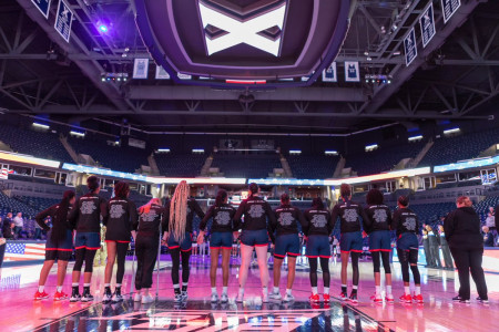 Players from the Xavier University Women's Basketball Team stand at midcourt wearing their commemorative Black Fives x BIG EAST warmup shirts.